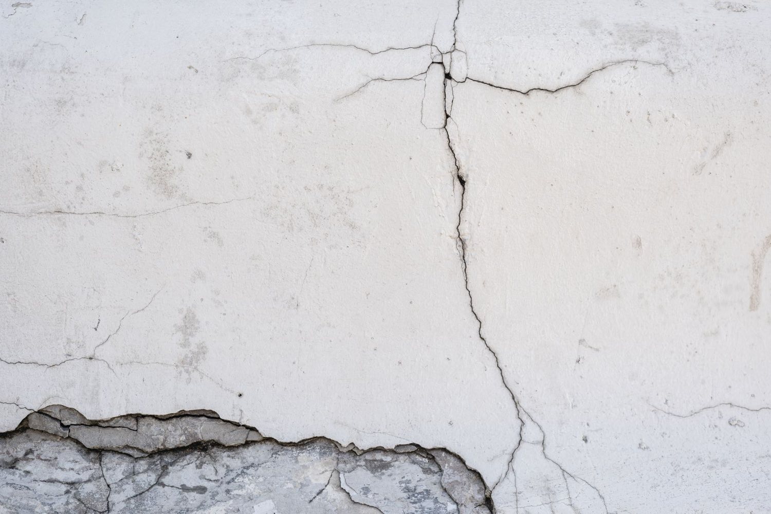 Cracks branching across a rendered exterior wall above spalling
